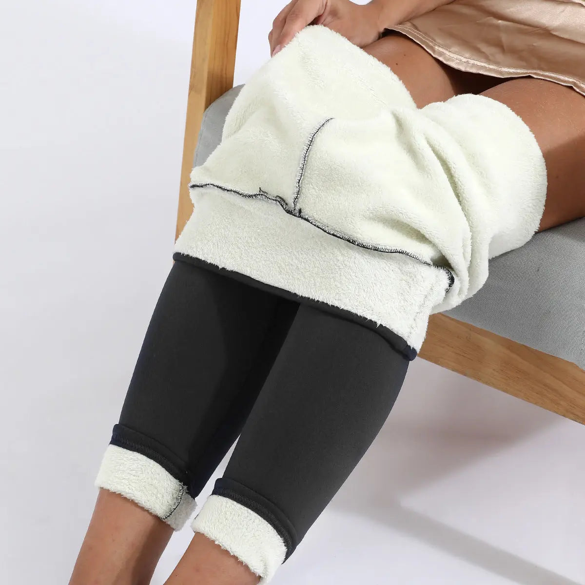 Donna seduta con pantaloni termici neri e coperta bianca in pile, su sedia grigia. Abbigliamento invernale, comfort, calore.