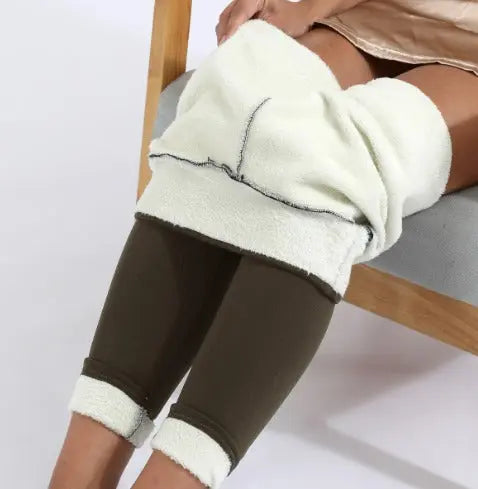 Donna seduta con coperta in pile bianca sulle gambe, indossa leggings marroni. Comfort, relax, abbigliamento casual, tessuto morbido.