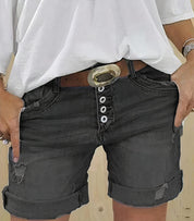 Shorts di jeans neri con bottoni, cintura con fibbia ovale, indossati con maglietta bianca. Moda casual estiva, abbigliamento donna trendy.