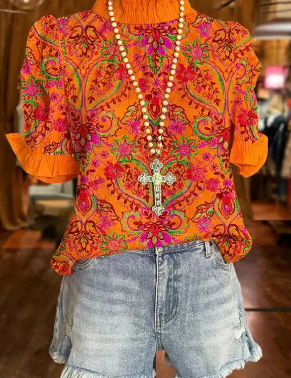 Maglietta arancione a fiori con collana croce, abbinata a shorts di jeans sfrangiati. Moda estiva, abbigliamento casual, stile boho chic.