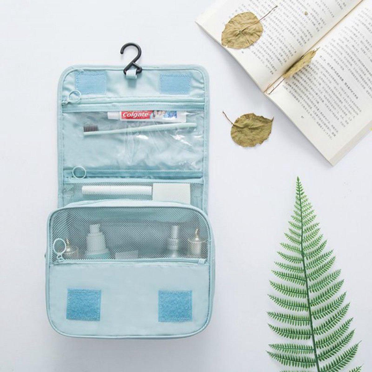 Borsa da viaggio azzurra aperta con gancio, contenente spazzolino Colgate, dentifricio e flaconi. Sfondo con libro aperto e foglie decorative.