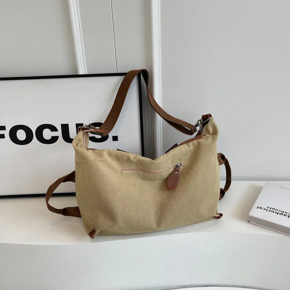 Borsa a tracolla beige in tela con cinghia marrone, tasca frontale con zip, su sfondo bianco. Accessorio moda casual e versatile.