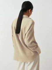 Donna di spalle con camicia beige a maniche lunghe, tessuto leggero, capelli neri raccolti in coda. Stile casual elegante, moda donna.