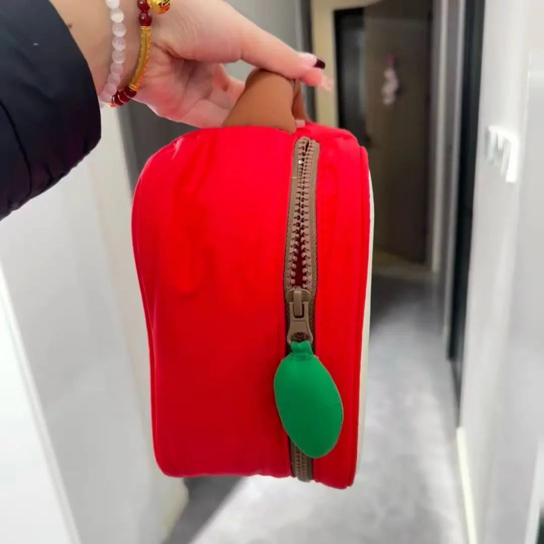 Borsa a forma di mela rossa con cerniera marrone e tiralampo verde, tenuta in mano. Design unico, accessorio moda, regalo originale.