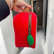 Borsa a forma di mela rossa con cerniera marrone e tiralampo verde, tenuta in mano. Design unico, accessorio moda, regalo originale.