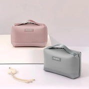 Due beauty case da viaggio in tessuto rosa e grigio con manico, etichetta "TRAVEL", ideali per organizzare cosmetici e accessori.