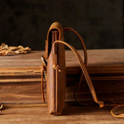 Borsa a tracolla in pelle marrone vintage su tavolo di legno, design sottile ed elegante, ideale per moda uomo e donna, accessorio di tendenza.