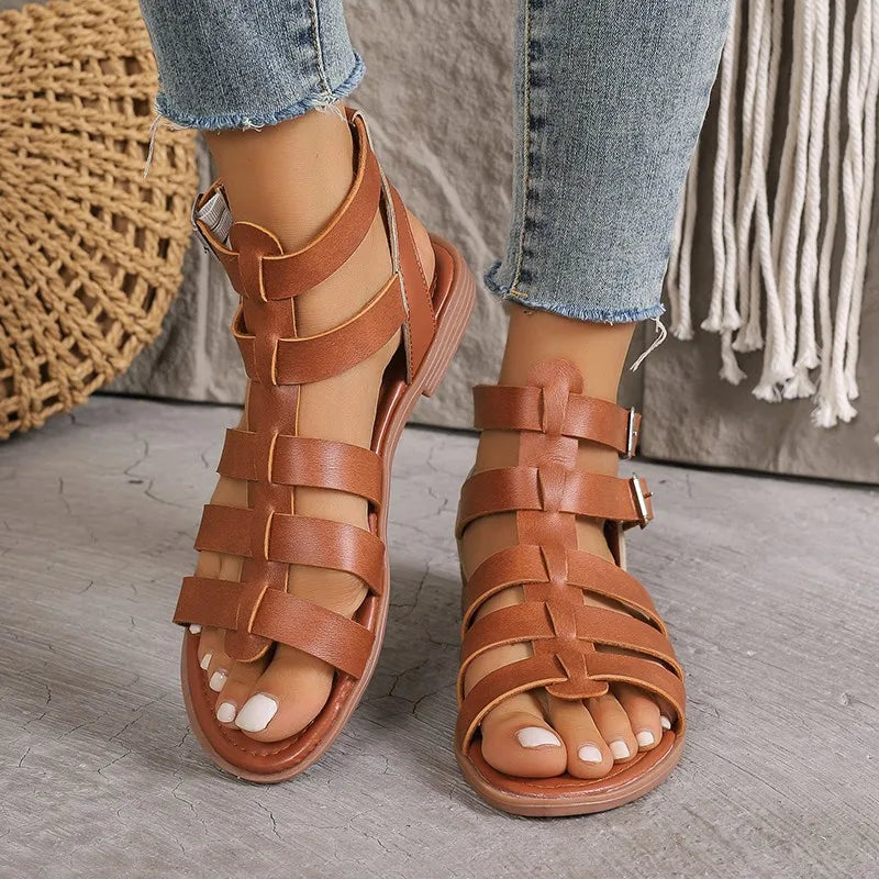 Sandali gladiatore in pelle marrone da donna, con cinturini incrociati e fibbie, indossati con jeans. Scarpe estive eleganti e casual.