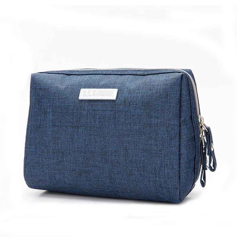 Astuccio da viaggio blu in tessuto, con cerniera e targhetta metallica. Ideale per organizzare accessori e cosmetici. Design elegante e funzionale.