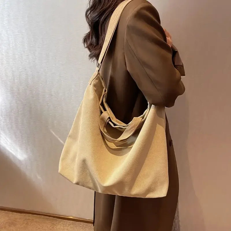 Donna con cappotto marrone indossa borsa a tracolla beige in tessuto, design minimalista, moda autunno, accessorio elegante e versatile.