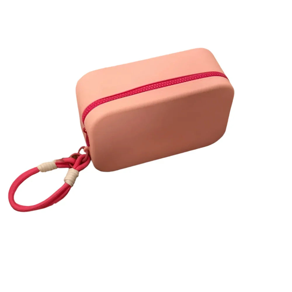 Custodia rosa in silicone con cerniera rossa e cinturino, ideale per protezione e trasporto di piccoli oggetti. Design compatto e resistente.