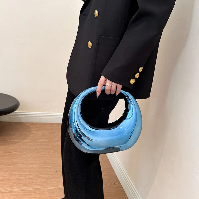 Borsa a mano blu metallizzata, design moderno e lucido, indossata da persona in abito nero elegante. Accessorio moda contemporaneo.