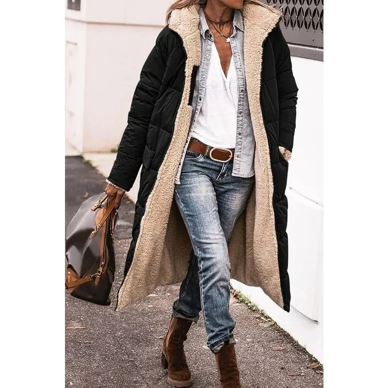 Cappotto lungo nero con interno in pelliccia sintetica beige, indossato con jeans e stivali marroni. Moda invernale donna, stile casual chic.