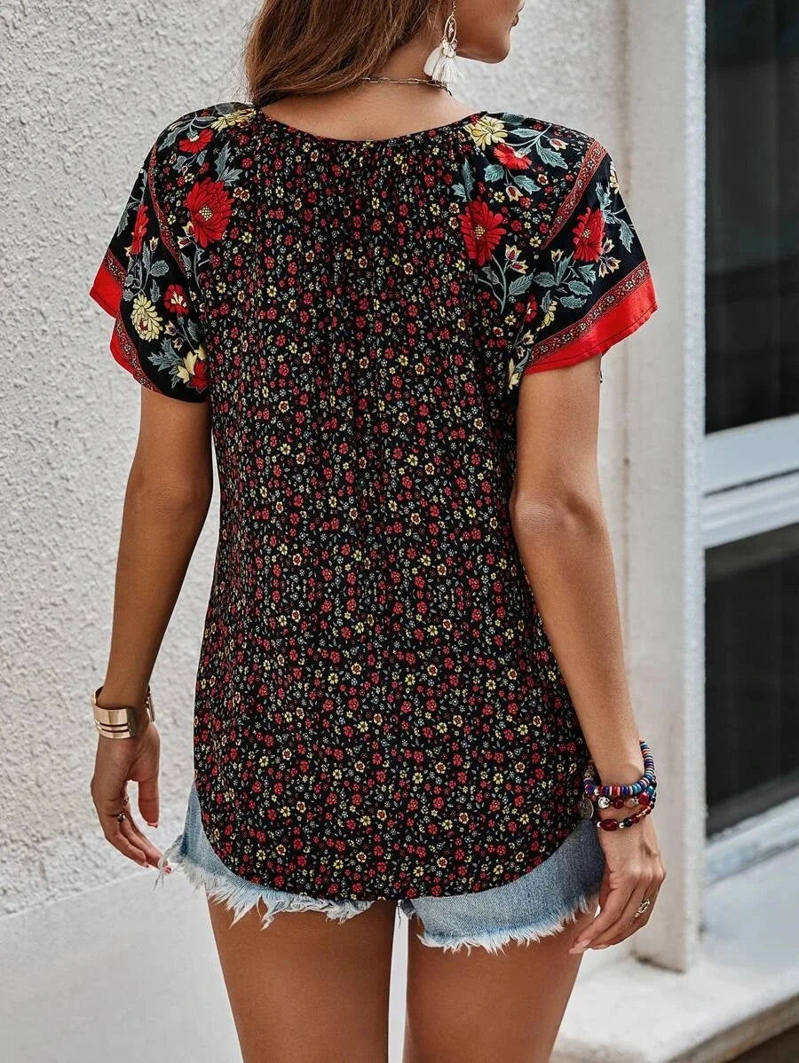 Donna con maglietta floreale nera e rossa, maniche corte, abbinata a shorts di jeans. Moda estiva casual, abbigliamento femminile trendy.