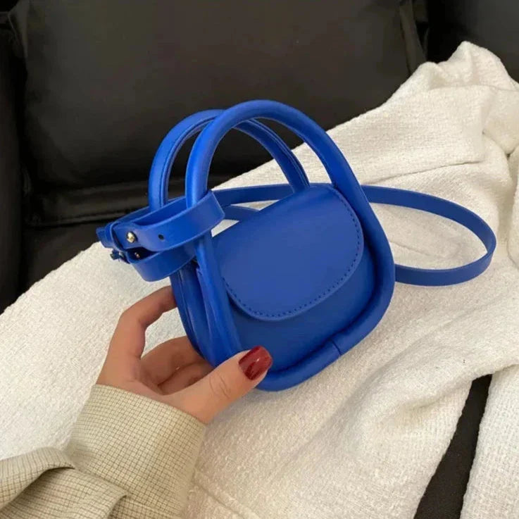 Borsa a tracolla mini blu in pelle, design moderno, chiusura a fibbia, su sfondo nero e bianco. Accessorio moda elegante e compatto.