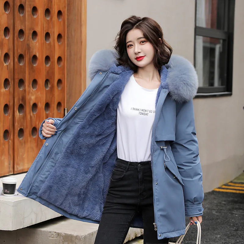 Giacca invernale donna blu con cappuccio in pelliccia sintetica, indossata da modella all'aperto. Moda femminile, abbigliamento caldo, stile casual.