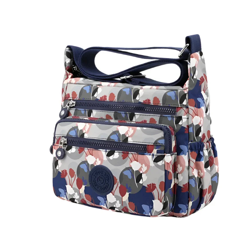Borsa a tracolla Kipling multicolore con stampa floreale, tasche multiple e chiusura zip. Design moderno e funzionale per uso quotidiano.
