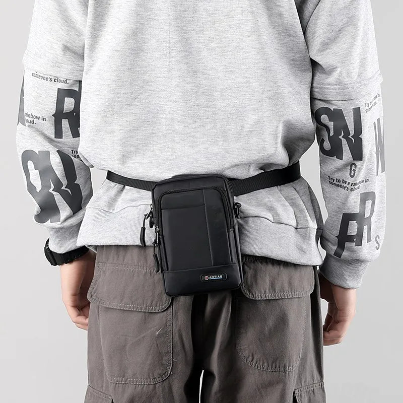 Uomo con marsupio nero in vita, indossa felpa grigia con scritte e pantaloni cargo marroni. Accessorio moda pratico e versatile per uomo.