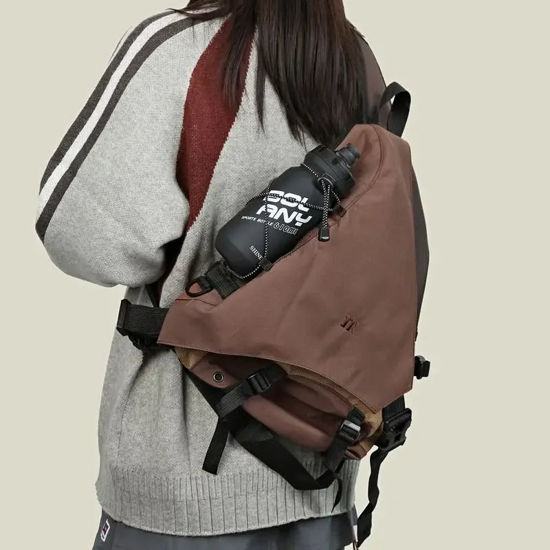 Zaino marrone con borraccia nera, indossato su giacca grigia e marrone. Accessorio outdoor, ideale per escursioni e attività sportive.