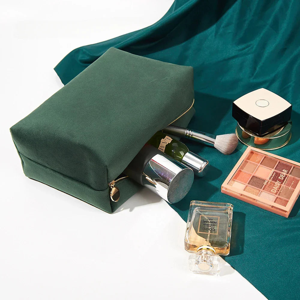 Astuccio verde in velluto con cerniera, contenente cosmetici: profumo, rossetto, pennello trucco, ombretto. Accessori bellezza eleganti e pratici.