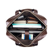 Borsa in pelle marrone aperta, vista dall'alto, con laptop, libri, quaderni e accessori. Elegante e spaziosa, ideale per lavoro e viaggio.