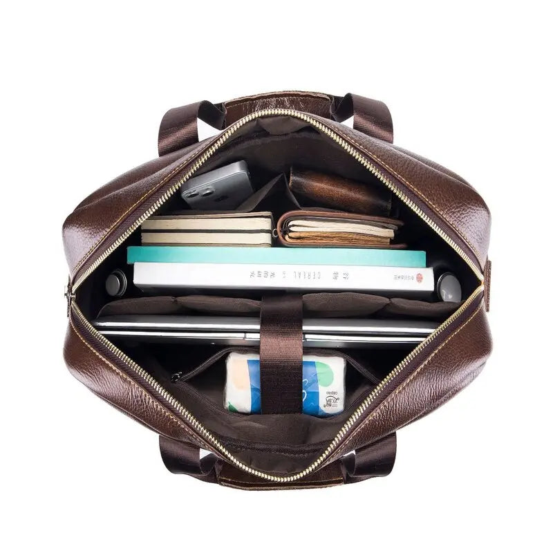 Borsa in pelle marrone aperta, vista dall'alto, con laptop, libri, quaderni e accessori. Elegante e spaziosa, ideale per lavoro e viaggio.