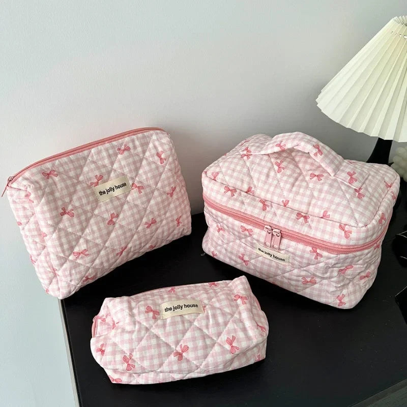 Set di tre beauty case trapuntati rosa con motivo a quadretti e fiocchi, ideali per organizzare cosmetici e accessori da viaggio.