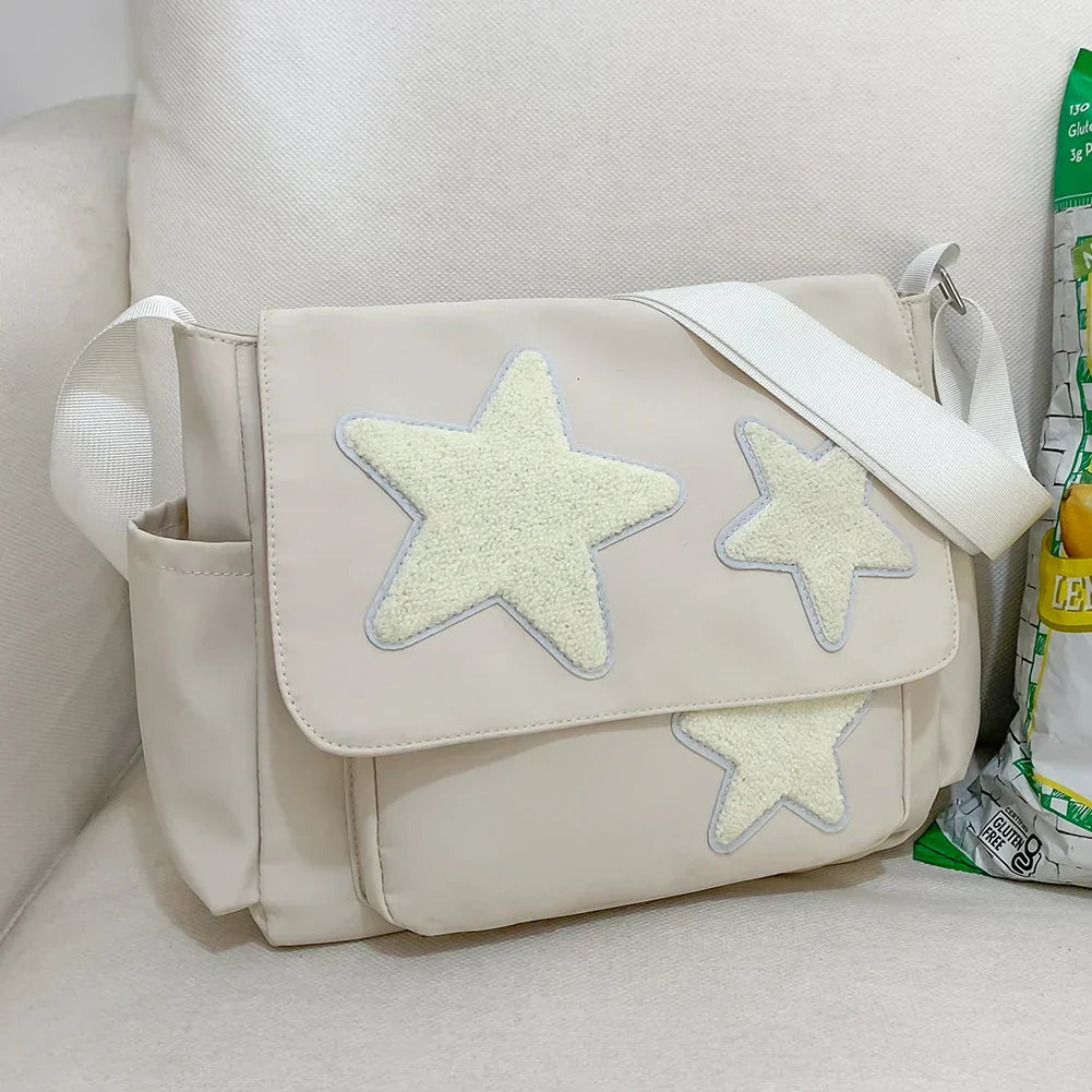 Borsa a tracolla beige con stelle decorative bianche, tasche laterali, su divano bianco. Accessorio moda casual, stile moderno.