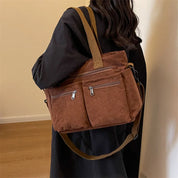 Donna con borsa a tracolla in velluto a coste marrone, tasche con zip, manici e tracolla regolabile, su sfondo interno. Accessorio moda casual.