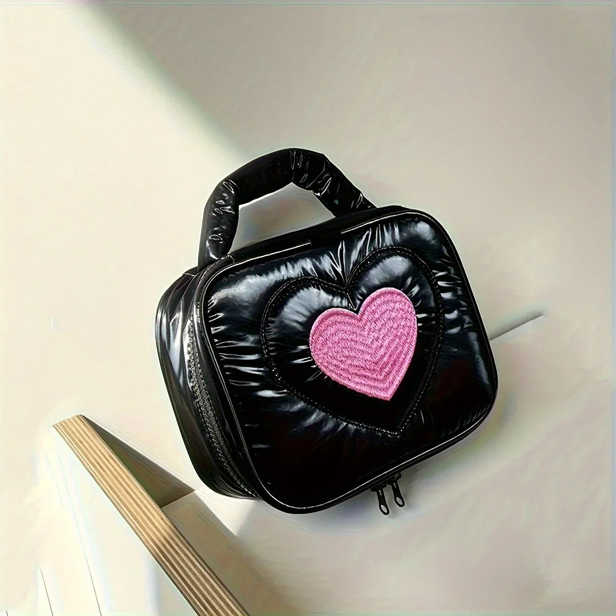 Borsa a mano nera lucida con cuore rosa centrale, design moderno, ideale per moda femminile. Accessorio trendy per ogni occasione.