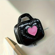 Borsa a mano nera lucida con cuore rosa centrale, design moderno, ideale per moda femminile. Accessorio trendy per ogni occasione.