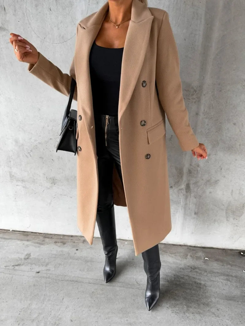 Cappotto lungo beige elegante, doppio petto, indossato con top nero, pantaloni in pelle e stivali. Look autunnale chic e moderno.