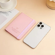 Custodia passaporto rosa con elastico accanto a smartphone bianco su tavolo beige. Accessori da viaggio eleganti e funzionali.