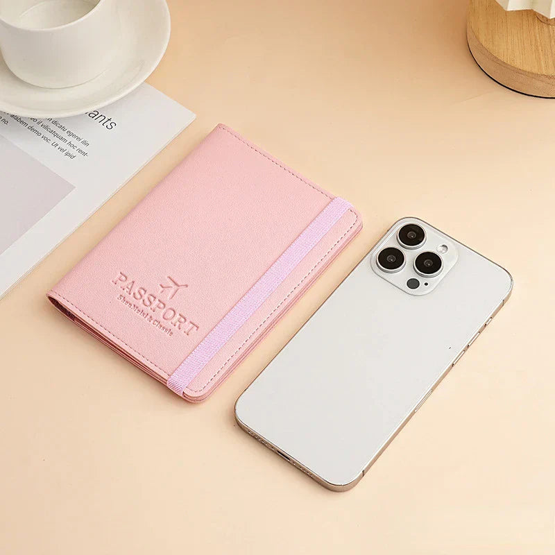 Custodia passaporto rosa con elastico accanto a smartphone bianco su tavolo beige. Accessori da viaggio eleganti e funzionali.