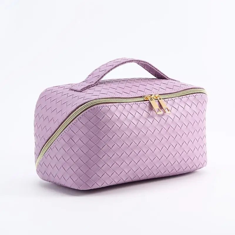 Borsa cosmetica intrecciata in pelle sintetica viola con cerniera dorata e manico superiore, ideale per trucco e accessori da viaggio.