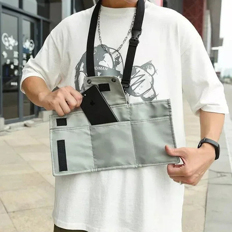 Uomo con borsa a tracolla grigia, tasche multiple, inserisce smartphone nero. Moda urbana, accessorio pratico per viaggi e quotidiano.