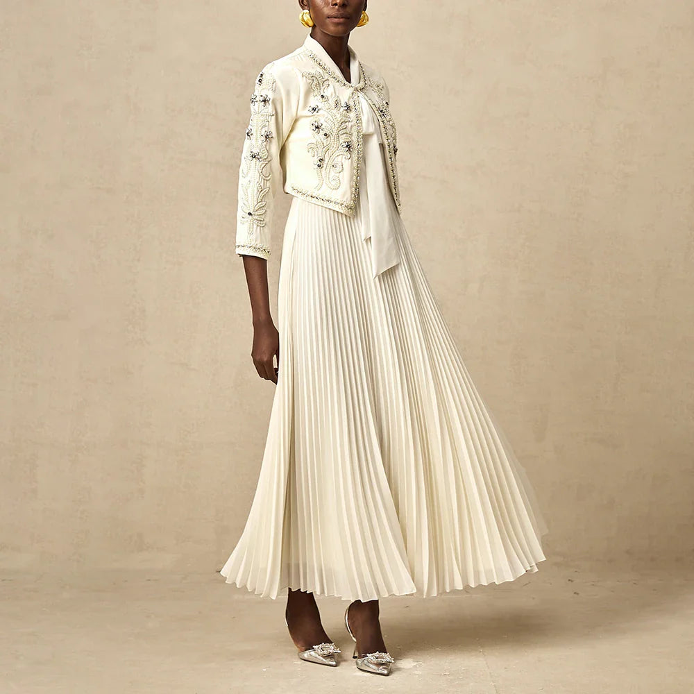 Abito lungo plissettato bianco con giacca ricamata, elegante e sofisticato, perfetto per cerimonie e occasioni speciali. Scarpe con tacco abbinate.