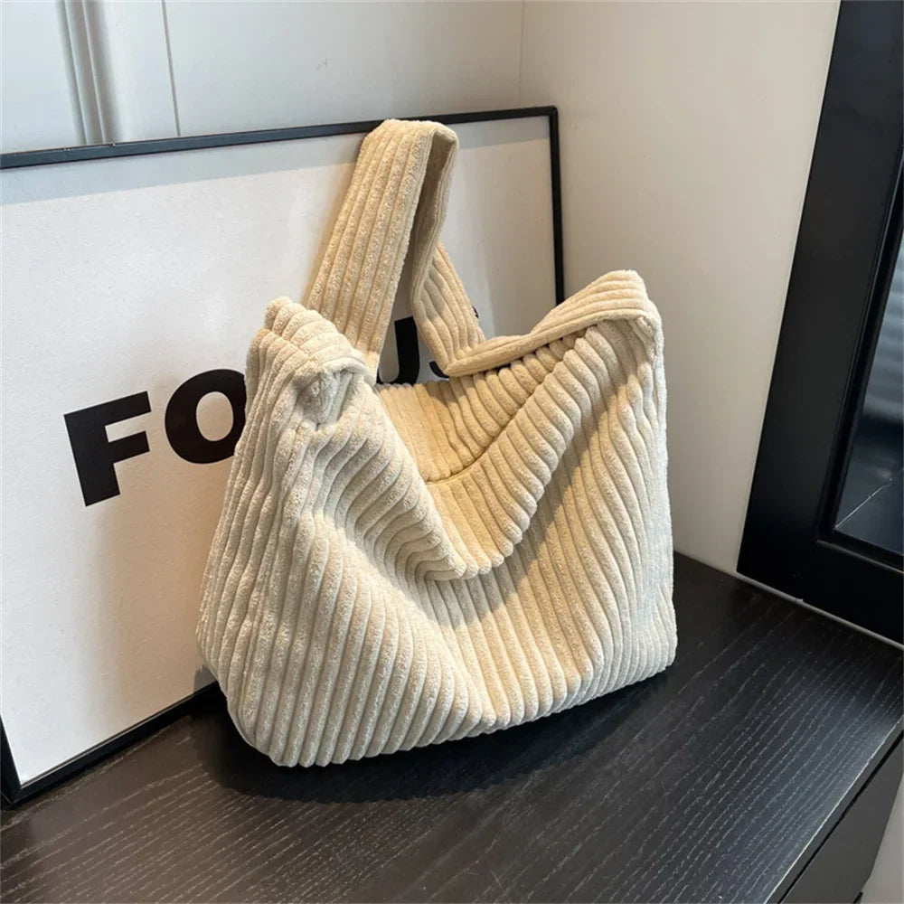 Borsa a spalla in velluto a coste beige su tavolo nero, design moderno e casual, perfetta per moda autunnale e invernale. Accessorio elegante e versatile.