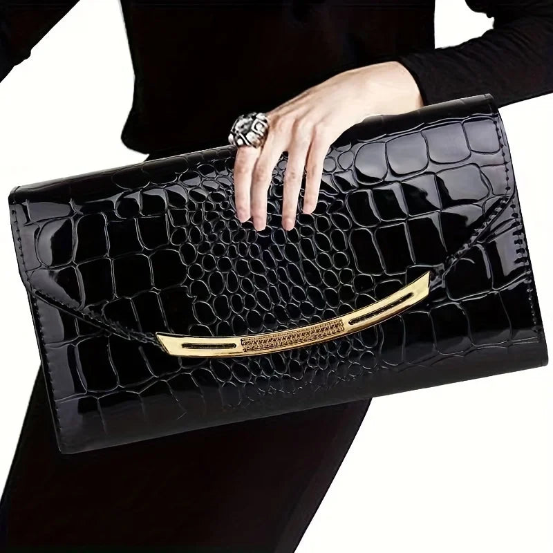Borsa clutch nera in pelle effetto coccodrillo, con dettagli dorati, tenuta da una mano femminile. Accessorio elegante e di lusso.