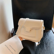 Borsa a tracolla bianca elegante su sedia nera, design minimalista, chiusura a patta, perfetta per moda femminile e accessori di tendenza.