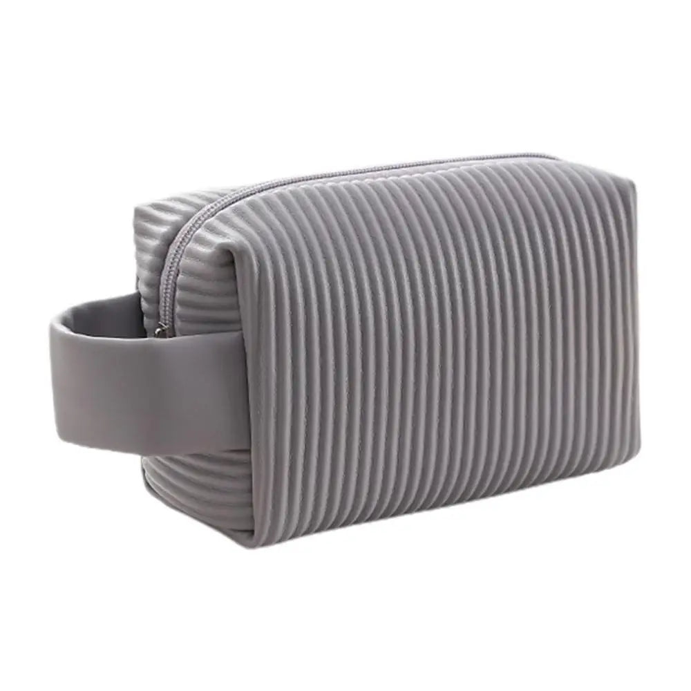 Astuccio da viaggio grigio con design a coste, manico laterale e chiusura a zip. Ideale per cosmetici e accessori. Elegante e funzionale.