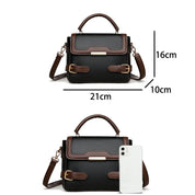 Borsa a tracolla in pelle nera e marrone, dimensioni 21x16x10 cm, con manico superiore e dettagli dorati, accanto a smartphone per confronto.