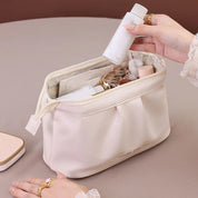 Borsa cosmetica bianca in pelle, aperta, con flaconi di prodotti per la cura della pelle. Mani femminili che inseriscono un flacone. Accessori da viaggio eleganti.