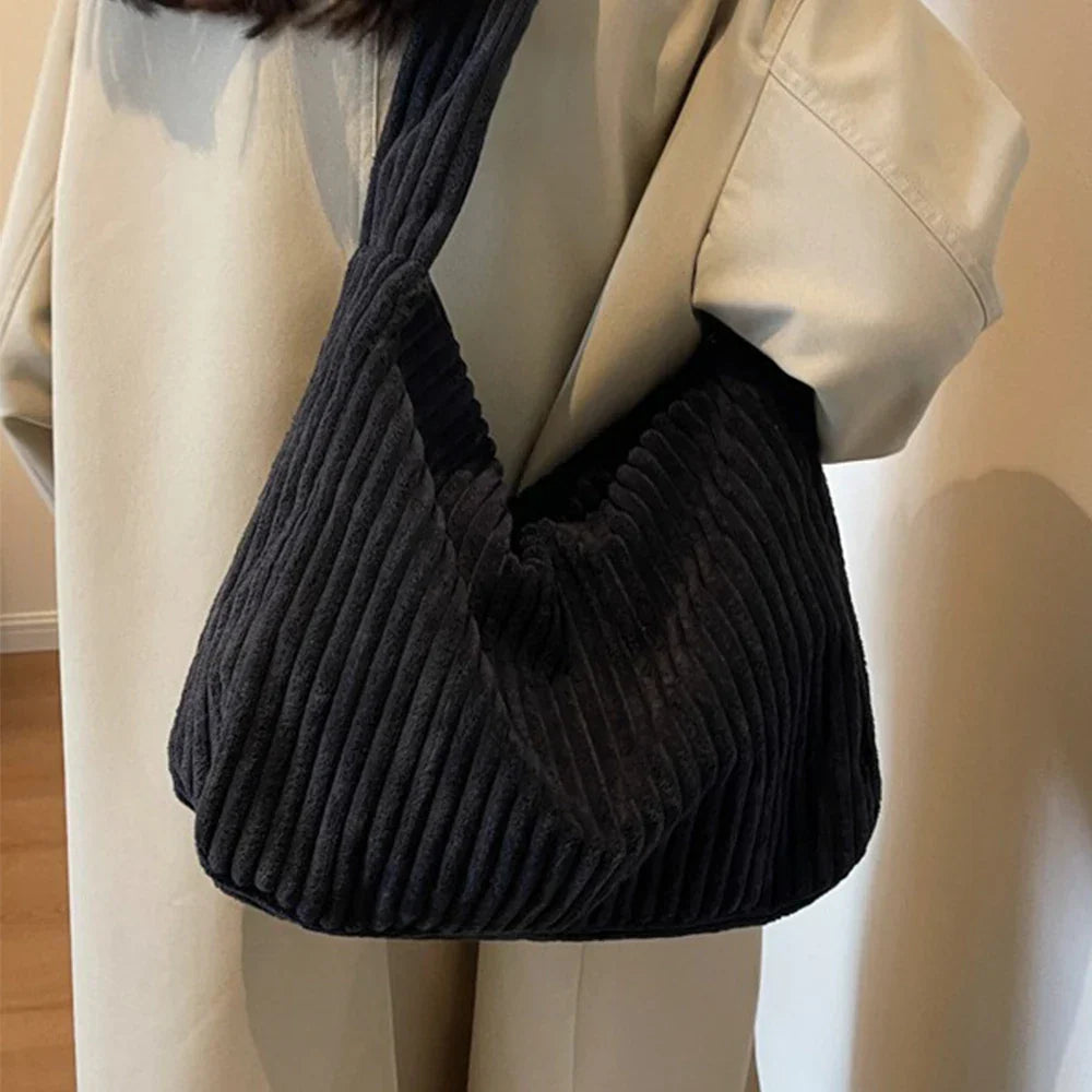 Borsa a spalla in velluto a coste nera, design moderno, indossata su cappotto beige. Accessorio moda donna, stile casual chic.