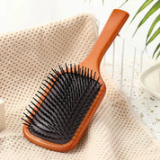 Spazzola per capelli in legno con setole nere su sfondo beige, ideale per districare e lisciare. Accessorio essenziale per la cura dei capelli.
