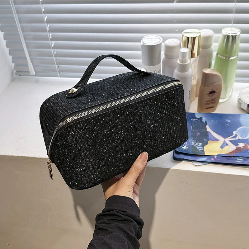 Astuccio cosmetico nero con cerniera, manico superiore, su mensola con flaconi di bellezza. Elegante e pratico per organizzare trucchi e accessori.