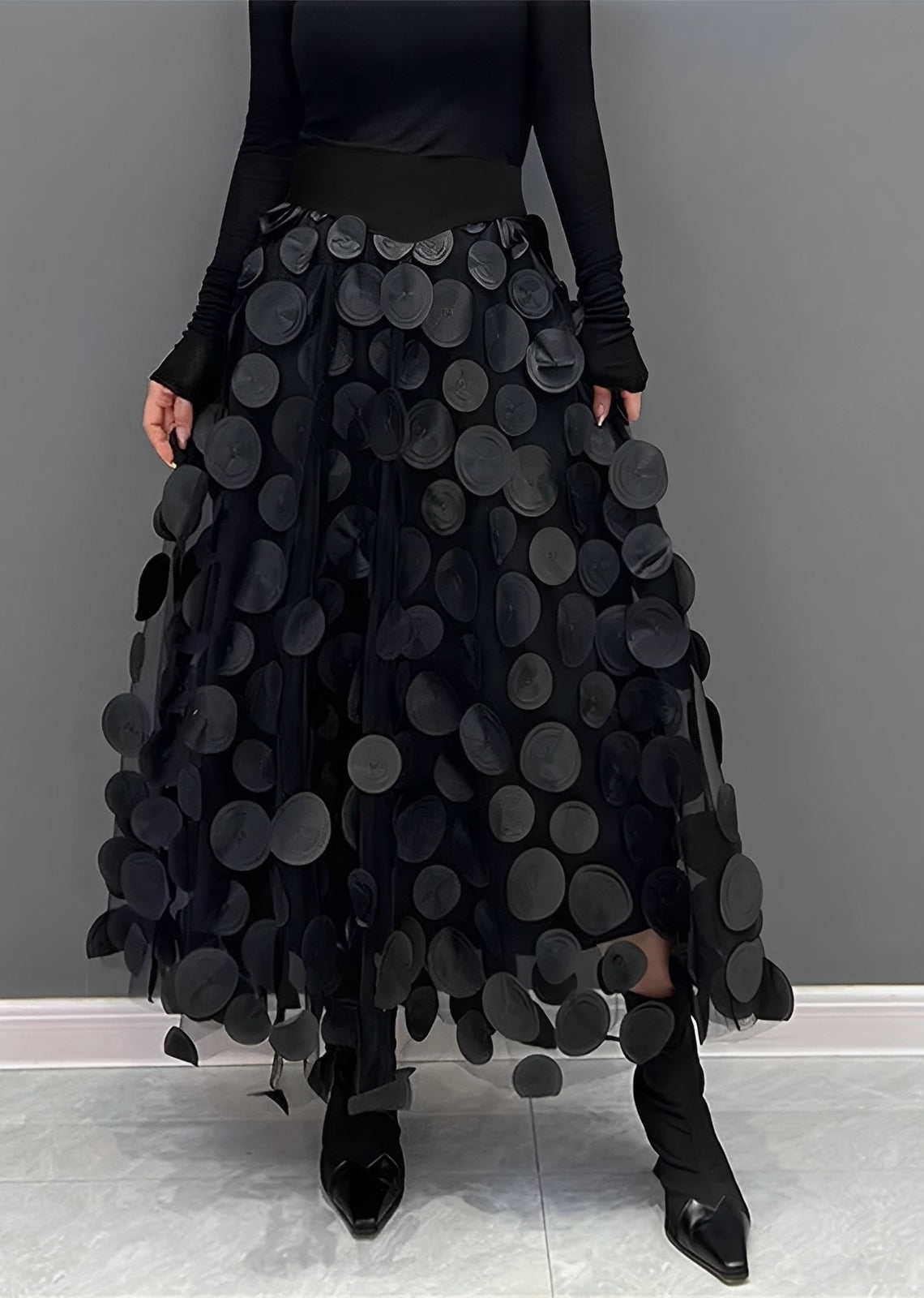 Gonna nera lunga con applicazioni circolari, indossata con stivali neri a punta. Design moderno ed elegante, perfetto per moda autunno/inverno.