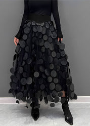 Gonna nera lunga con applicazioni circolari, indossata con stivali neri a punta. Design moderno ed elegante, perfetto per moda autunno/inverno.