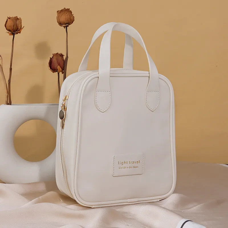 Borsa da viaggio bianca elegante con manici, design minimalista, accanto a vaso decorativo e fiori secchi, su sfondo beige. Accessorio moda pratico.