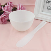 Ciotola bianca in plastica con spatola su sfondo rosa, decorata con rose e cornice. Accessori per cosmetici, cura della pelle, bellezza.